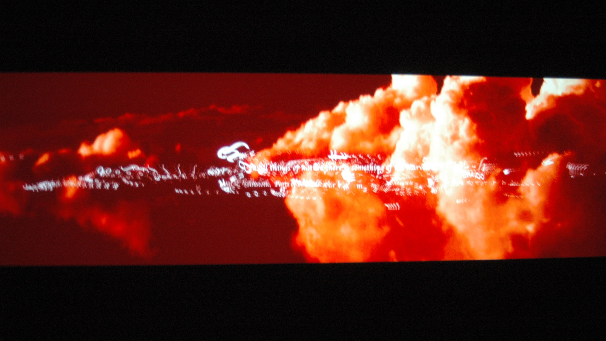 Red tinged clouds with illegible words in white script font across them projected on screen.