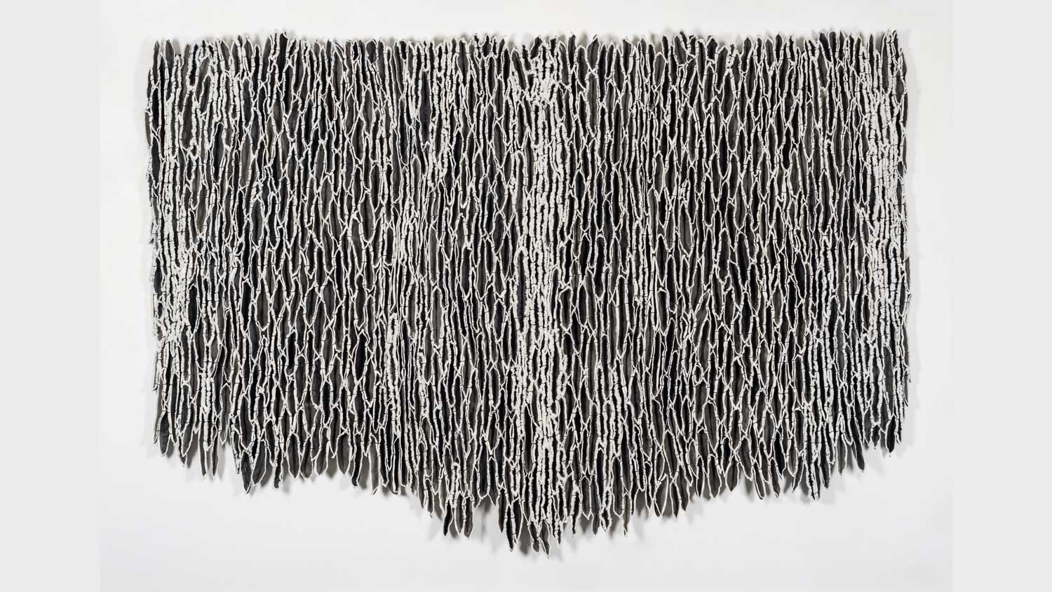A black and white bark like wall hanging on a blank white wall. 