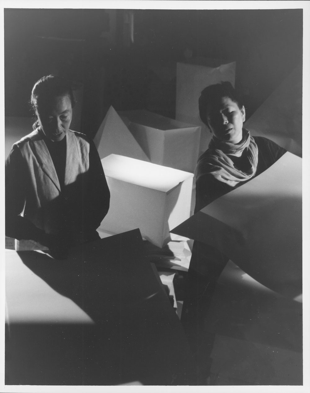 Two Japanese women standing amongst geometric sculptures  of various sizes. 