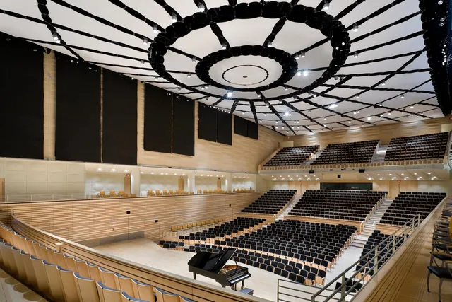 a view of the concert hall looking from the choir loft across to the balcony. a shiny black steinway grand on the stage. a fabric ceiling extends above like the sails of a ship.