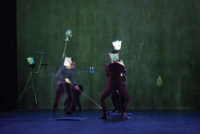 Two performers in black manipulating an assortment of human-esque sculptures. 