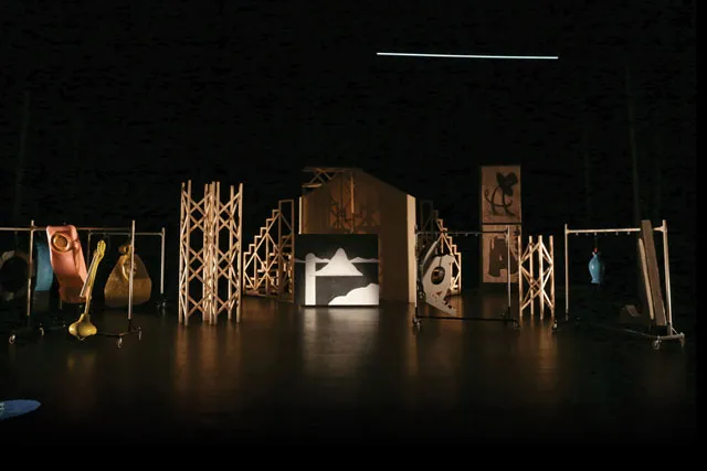  A dark stage with various abstract wooden set pieces placed thought the space. 