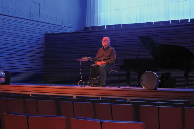 Johannes Goebel seated on the concert hall stage in blue and red light. 