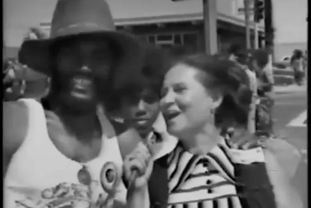 a black man and white woman in the streets at a festival in 70s era clothing. 