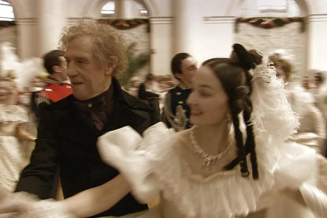 An older man and young woman dancing in crowded ballroom 19 century attire. The couple is blurred in motion. 