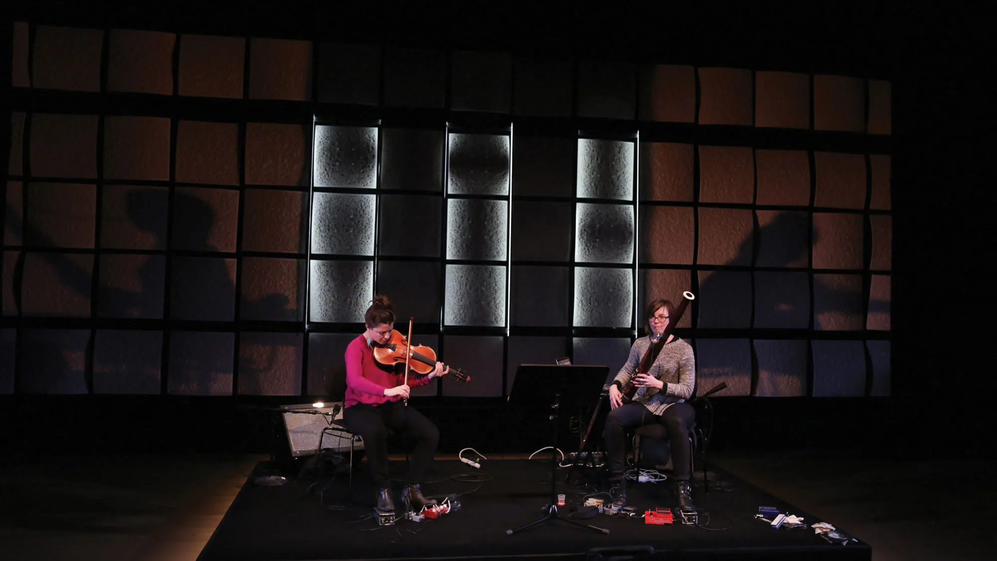 two woman on stage playing instruments in a black box studio. 