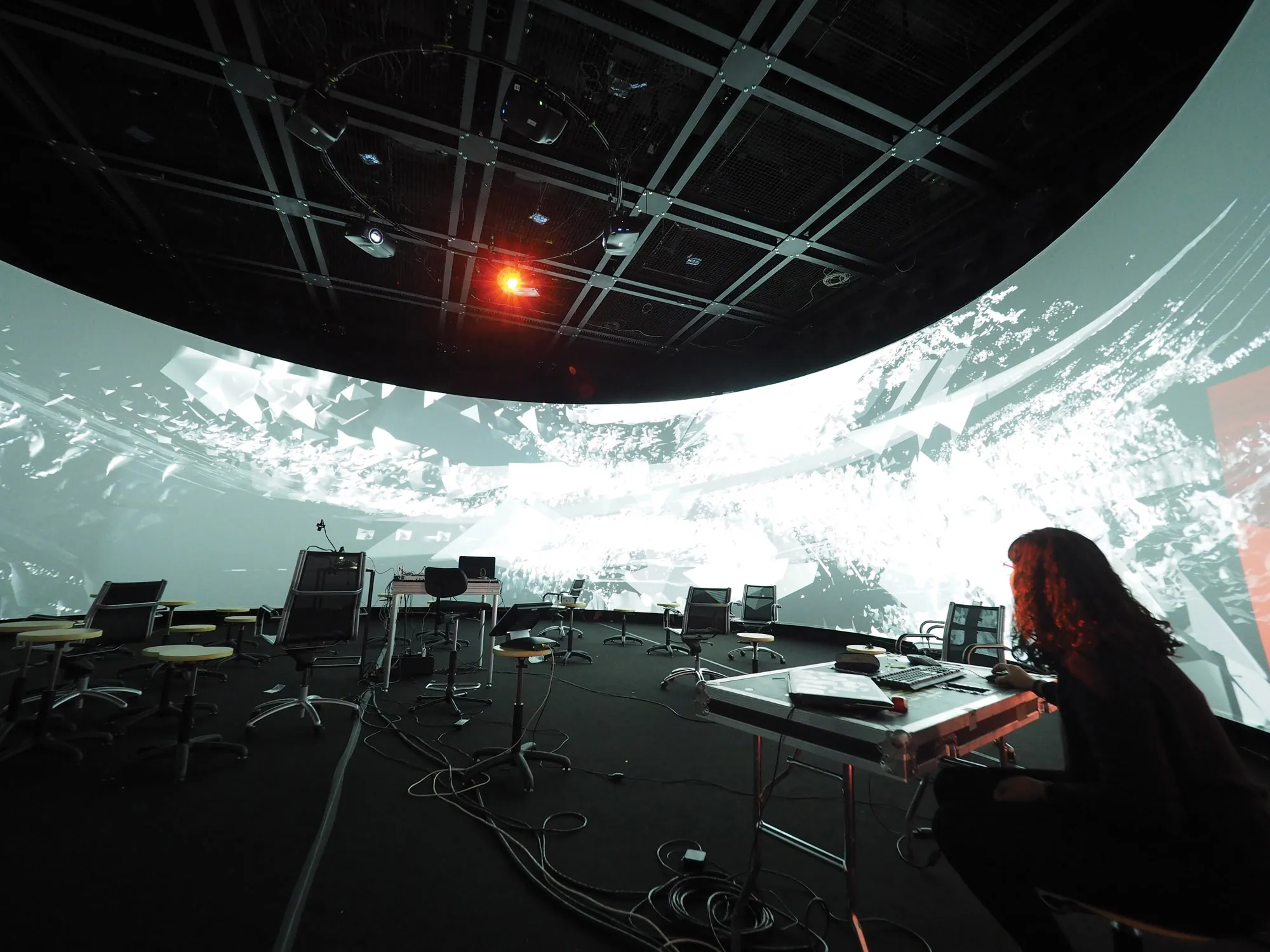 laura luna seated behind a table in a room cluttered with various cables and tech gear in the middle of a 360 panoramic screen. 