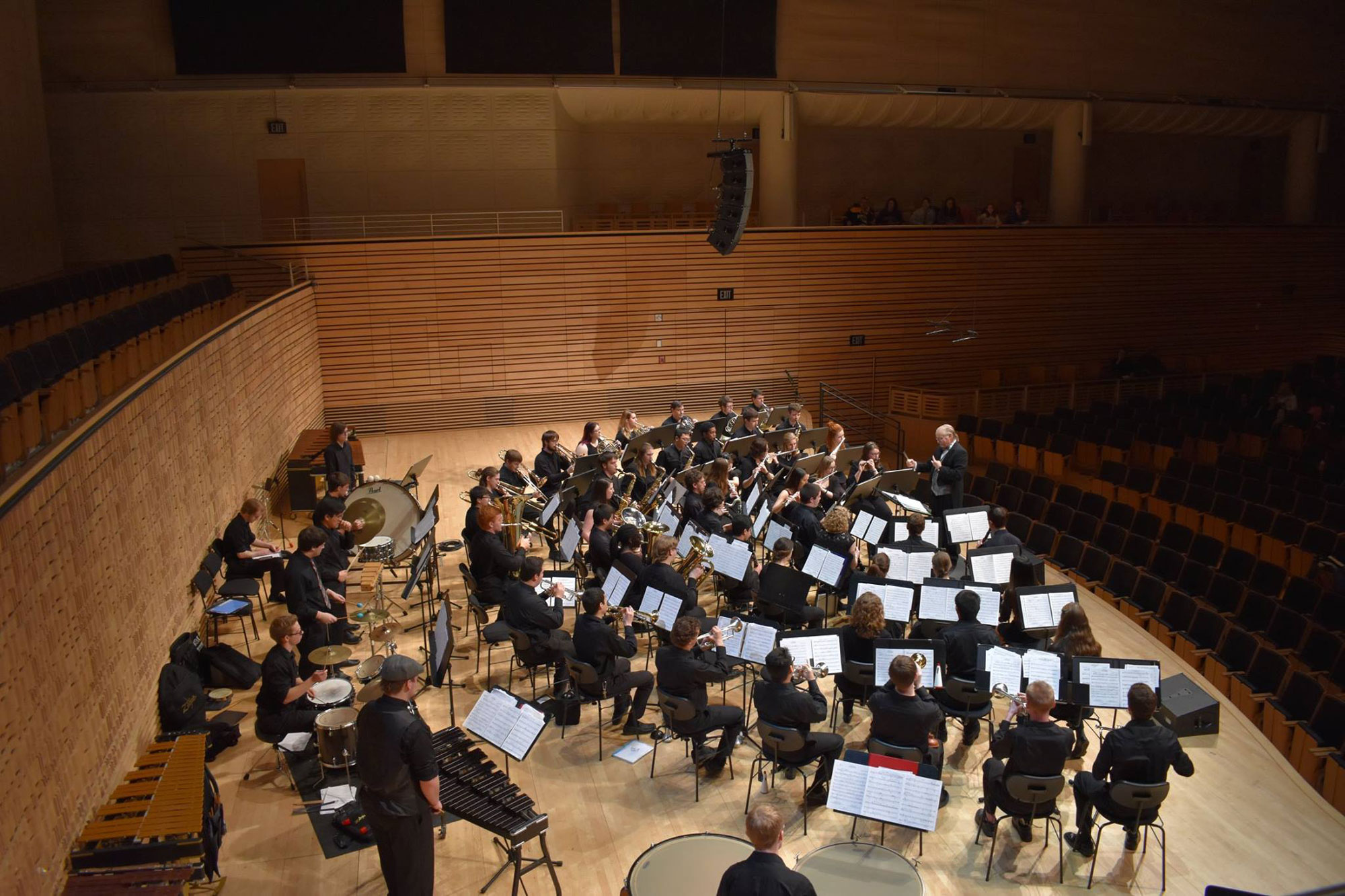 An orchestra seated in a semi circle in dress rehearsal in an empty concert hall. 