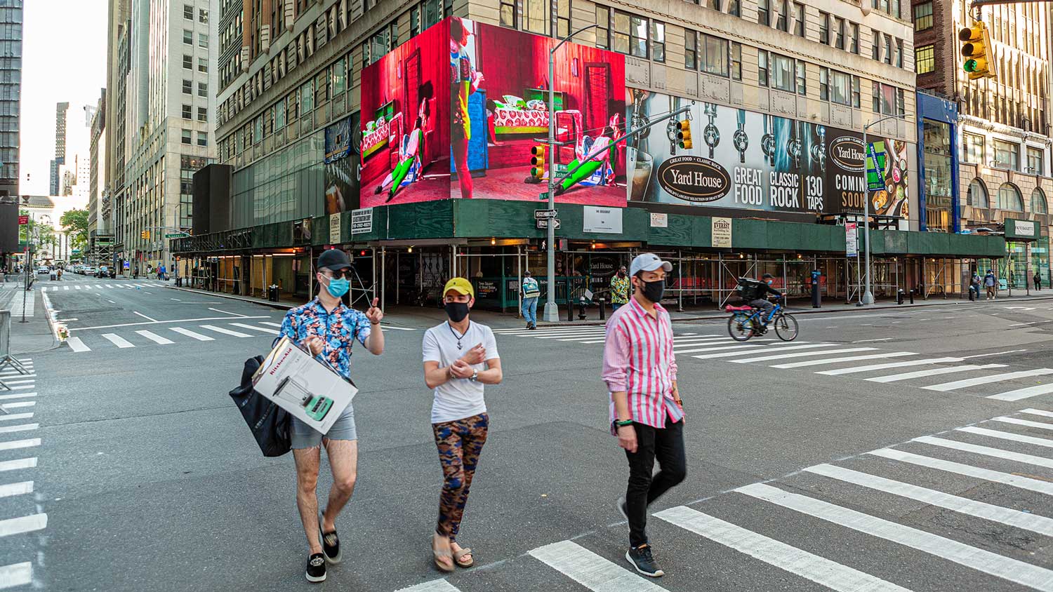 Three men walking through times square with masks on, a projection in the background of the dance film ward of the feral horses. 