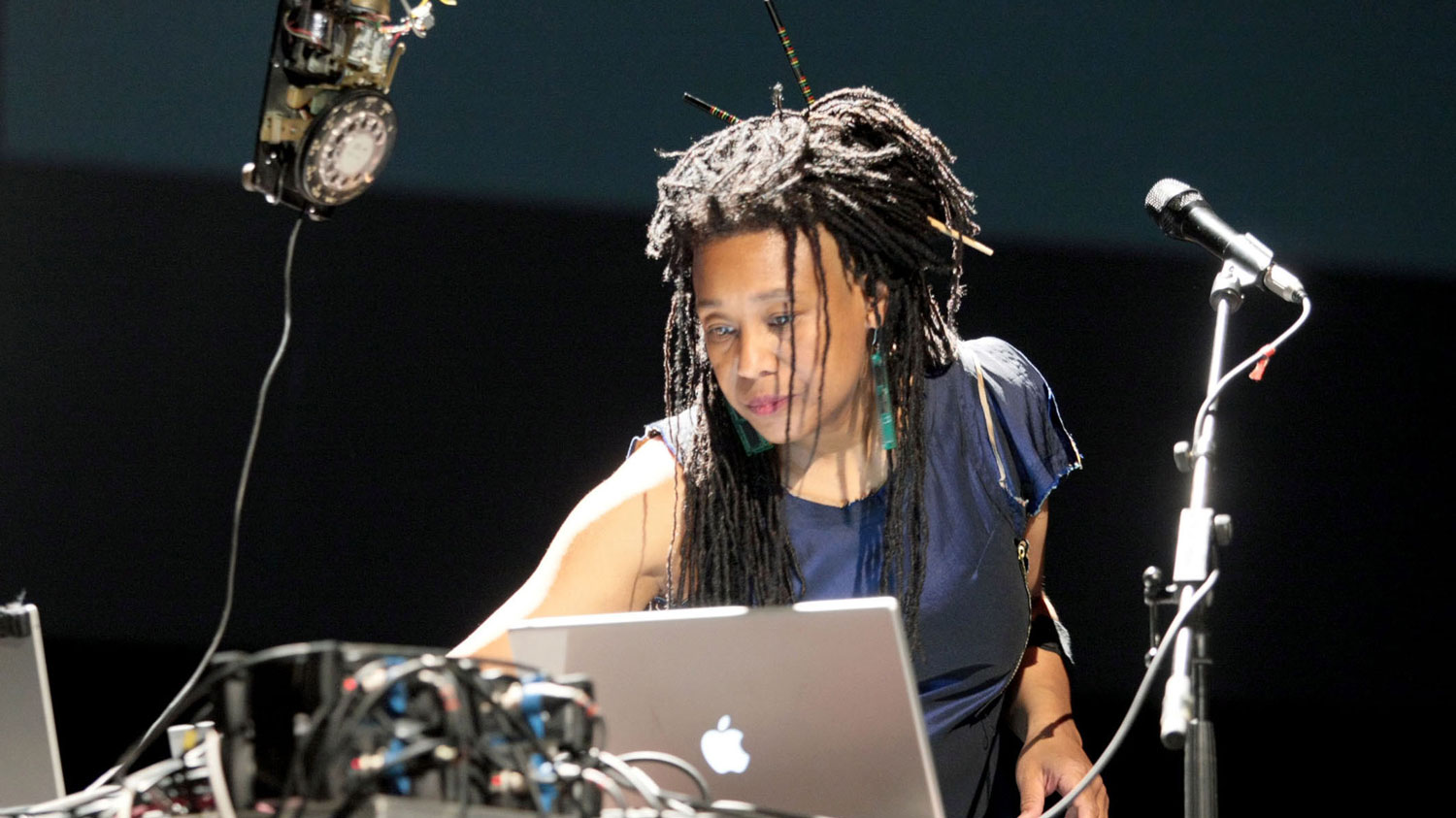 PamelaZ reaching across a lap top next to a microphone focused on the task in front of her. 