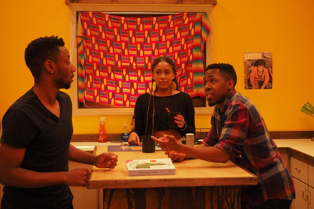 Chris Jarrell, Nozipho Mclean and Eric Lockley seated around a table in a warm, yellow room with a colorful window covering. 