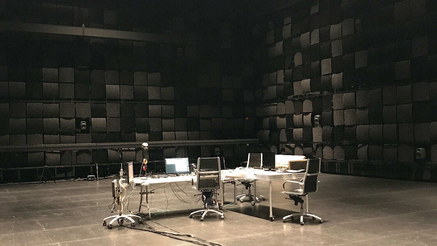 A cluttered conference table with three chairs in the middle a black box theater. 