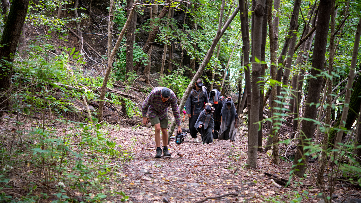 four actors walk on a leafy path toward a steadicam in a deciduous forest