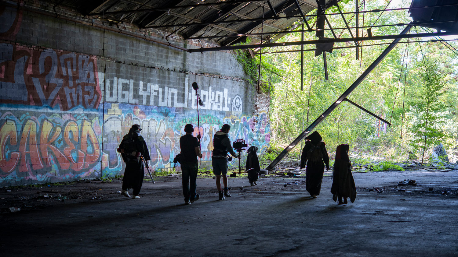 a group of people walking in a old post-industrial building, followed by a steadicam operator.