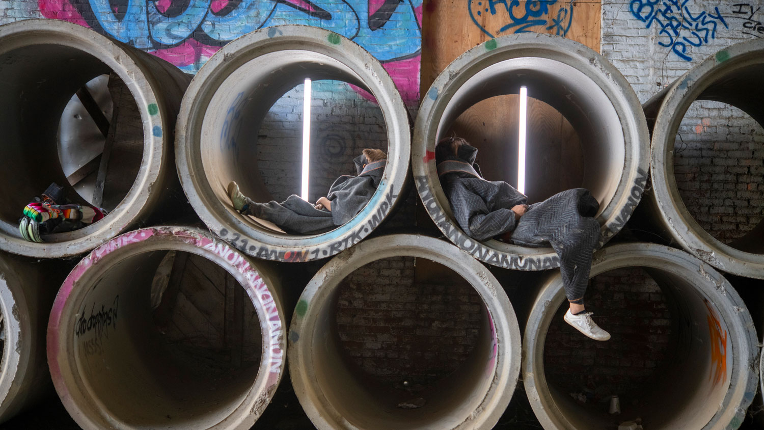 two people laying inside concrete water pipes against a graffiti wall