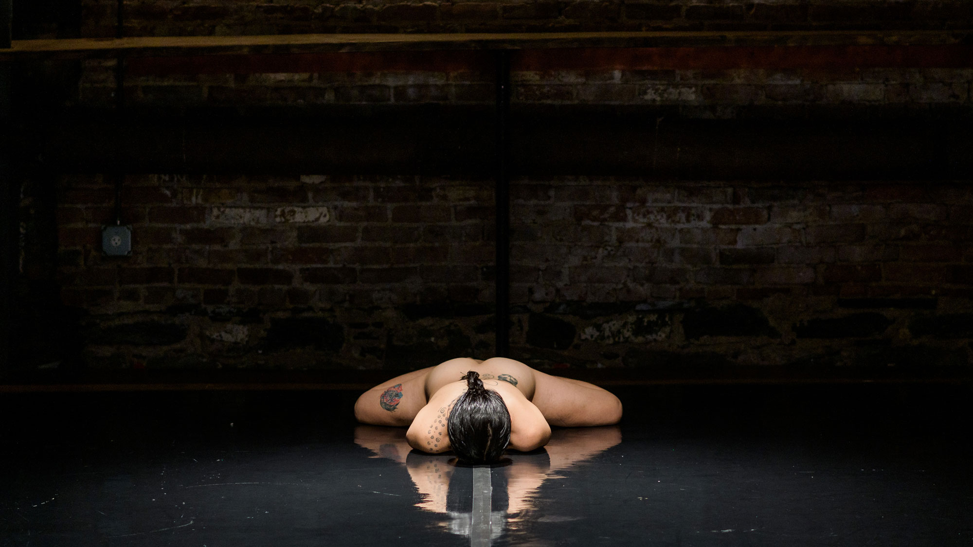 a nude woman on a black stage laying face down with arms under her body