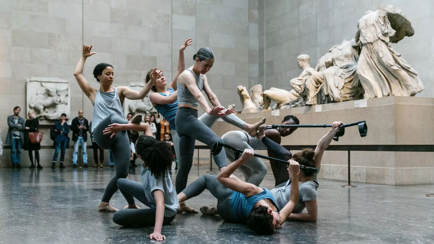 a group of dancers performing in front of a group of greek statues in a museum