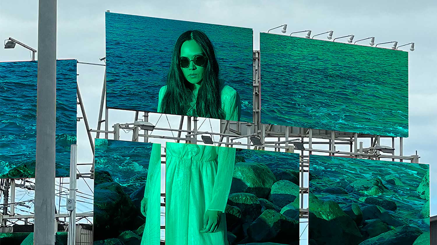 an asian woman in a green tint printed across two city billboards, with ocean shore in the background.