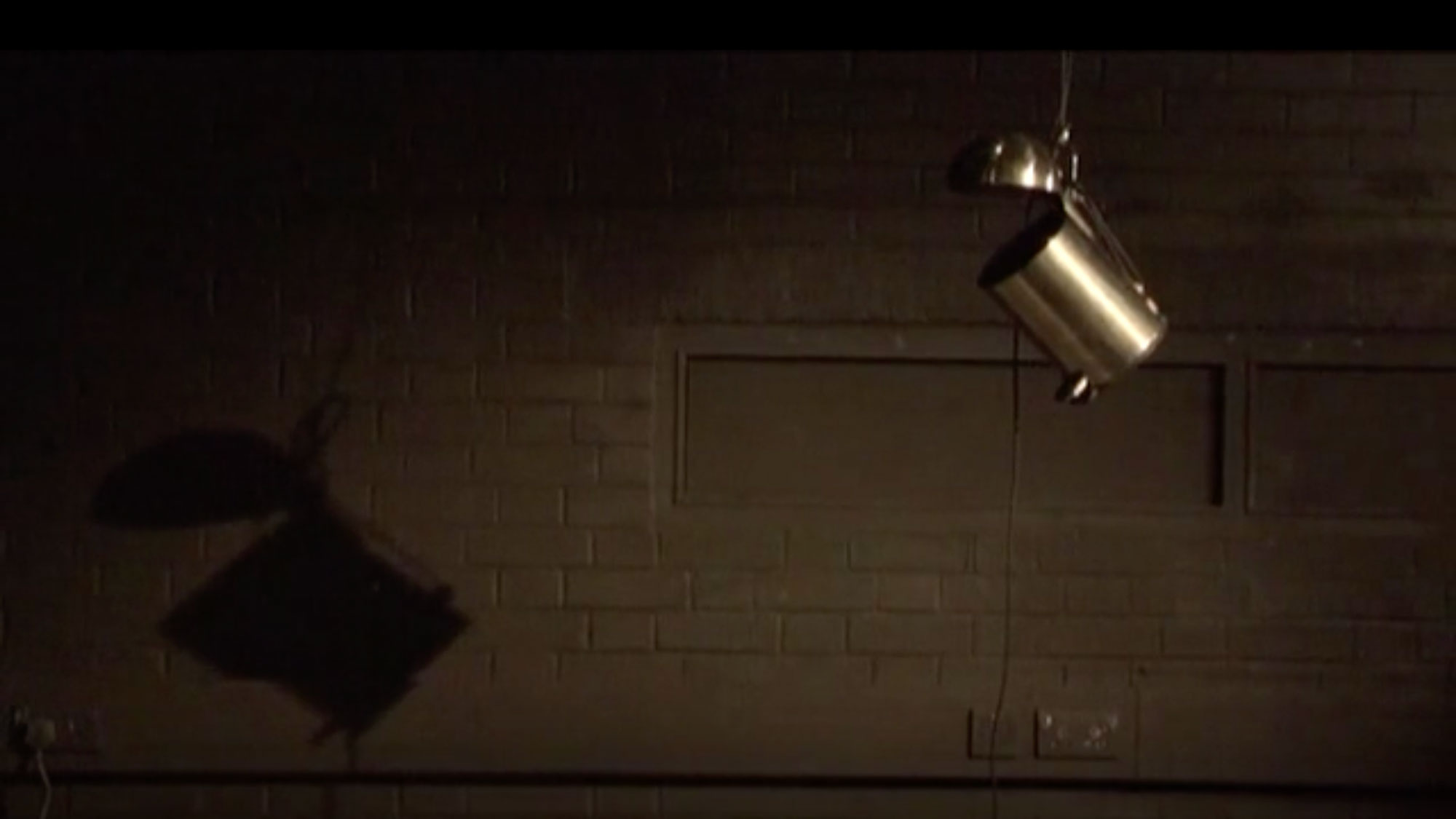a small silver trash can hangs from a ceiling in a dark studio