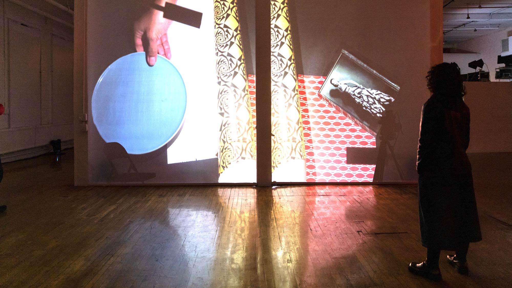 a woman stands in shadow looking at a video projected on a wall in front of them.