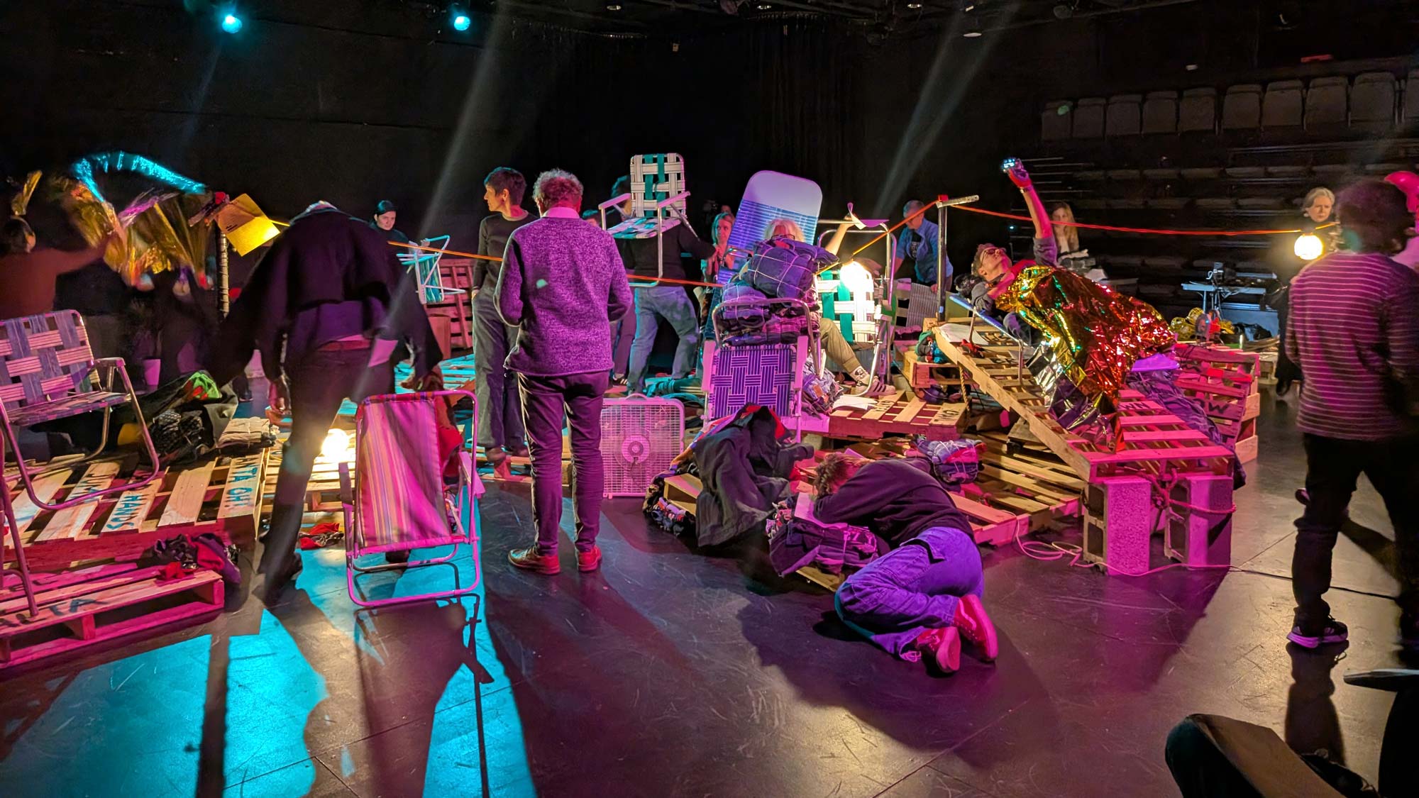 various people circling a pile of pallets and and other various objects in a black box studio