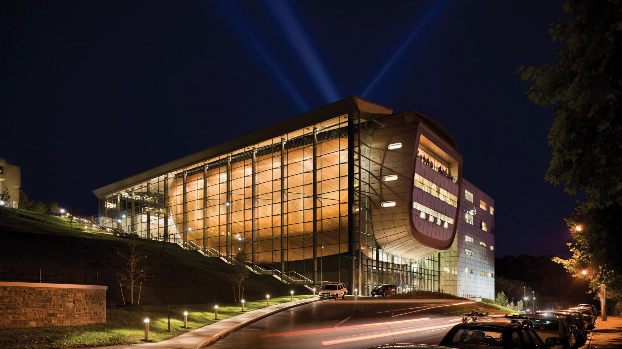 The exterior of EMPAC light from within at night with cars on 8th street passing as blurry of light. 