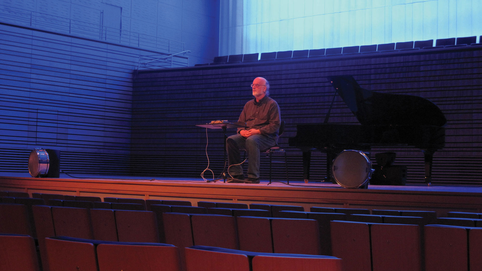 Johannes Goebel seated on the concert hall stage in blue and red light. 