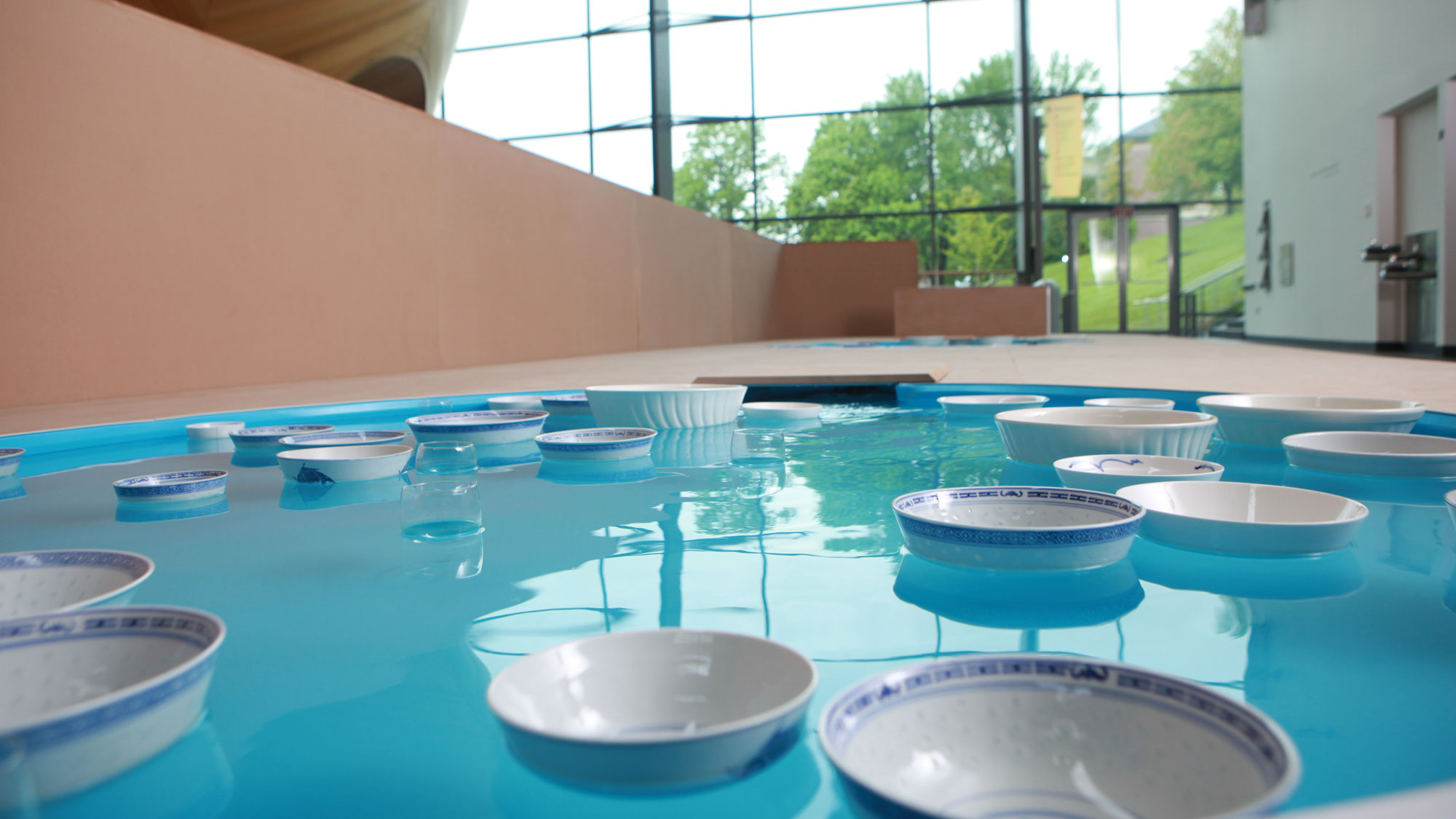 Numerous blue and white porcelain bowls floating in a blue pool on the mezzanine the interior of EMPAC. 