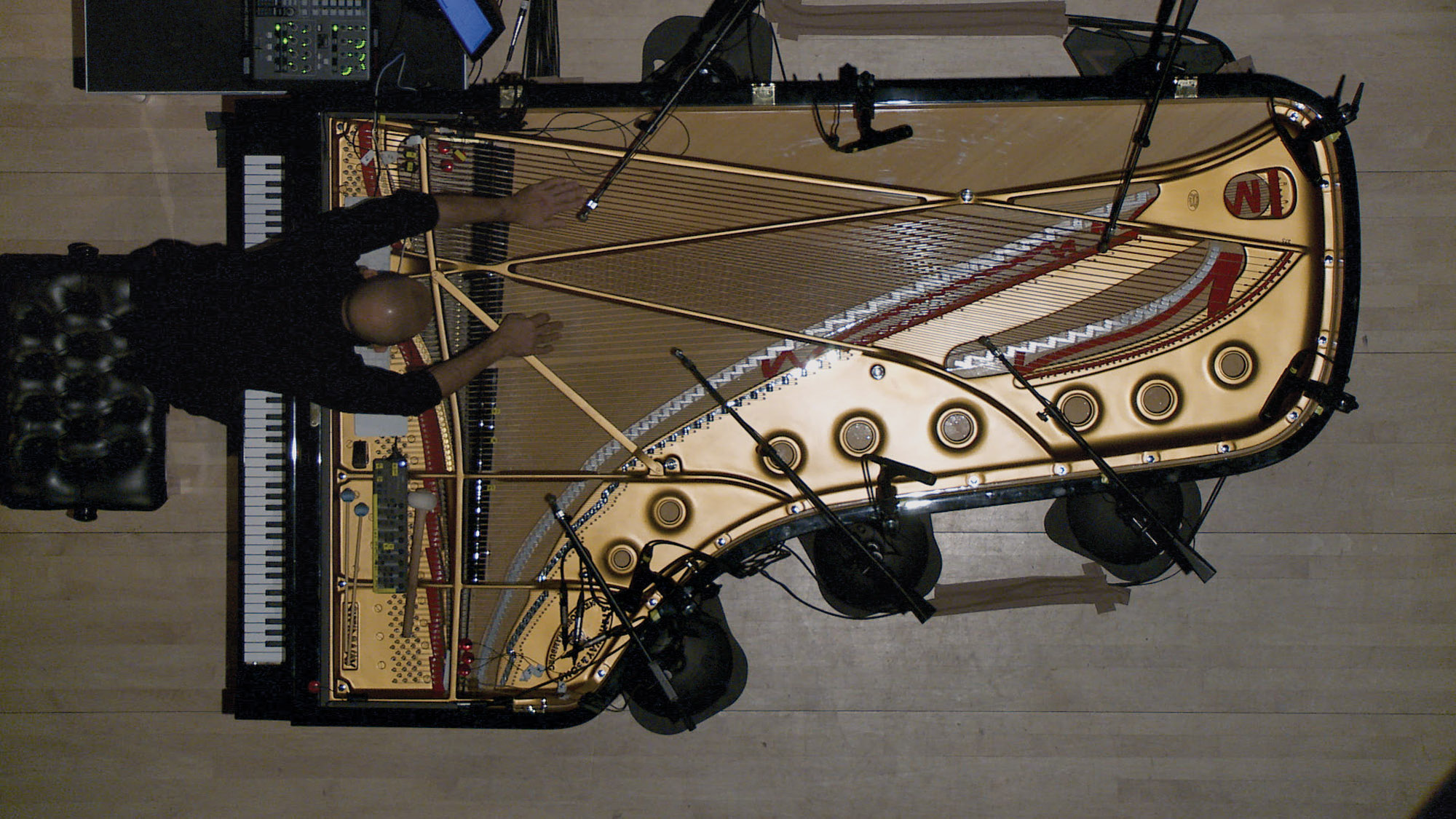 An aerial view of a man leaning over an open grand piano, plucking at its strings. 