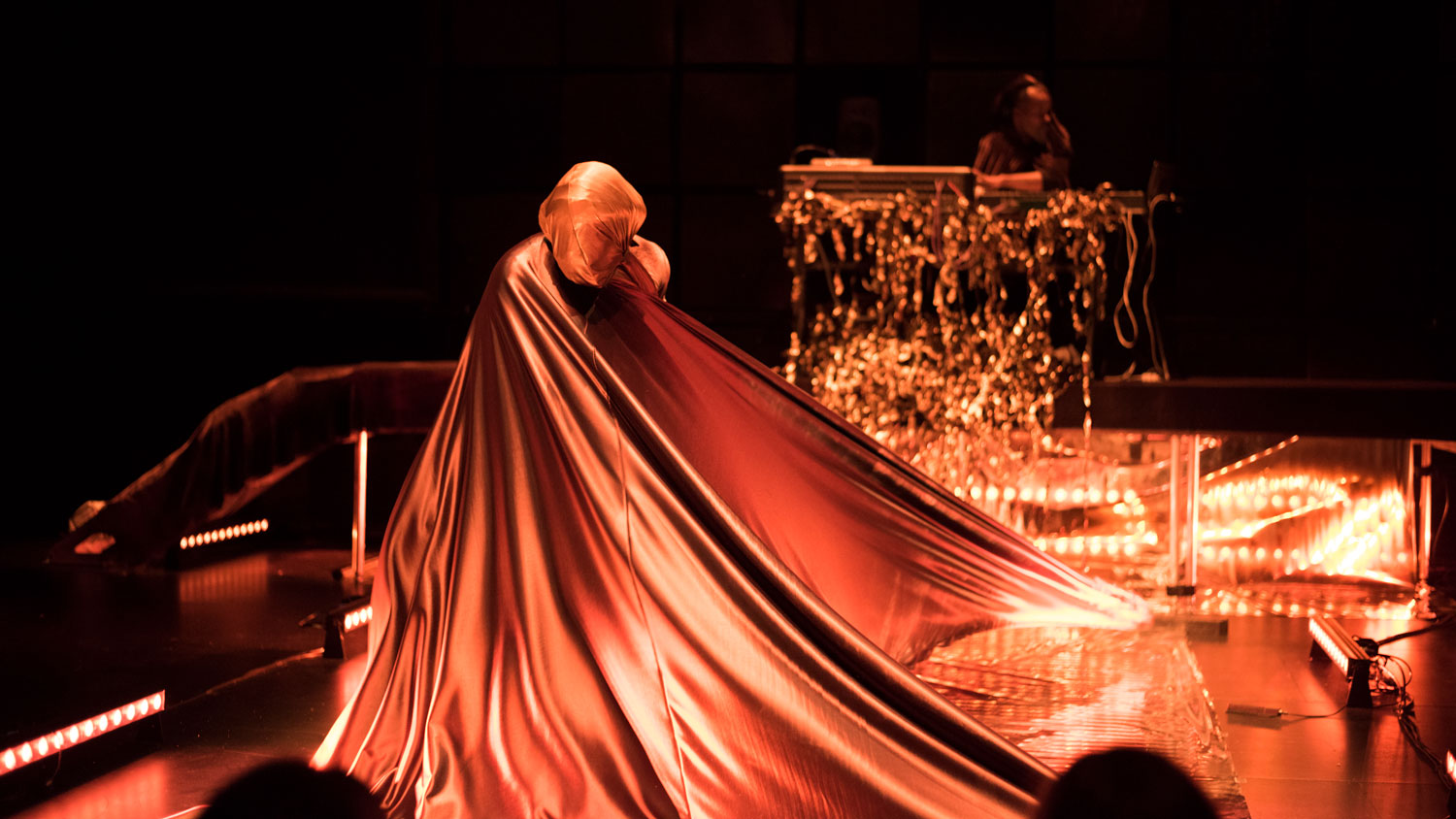 An human fully draped in cognac colored satin fabric twisting on a warmly lit stage. 