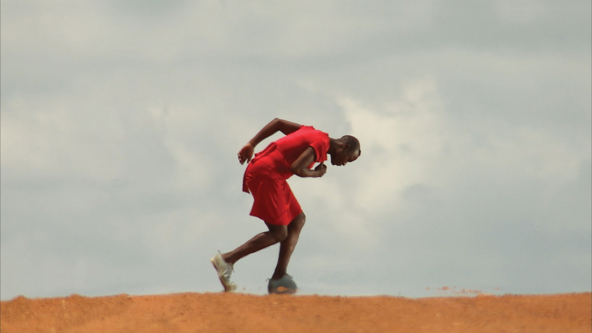 A Black person wearing red hunched in motion in a desert scene. 