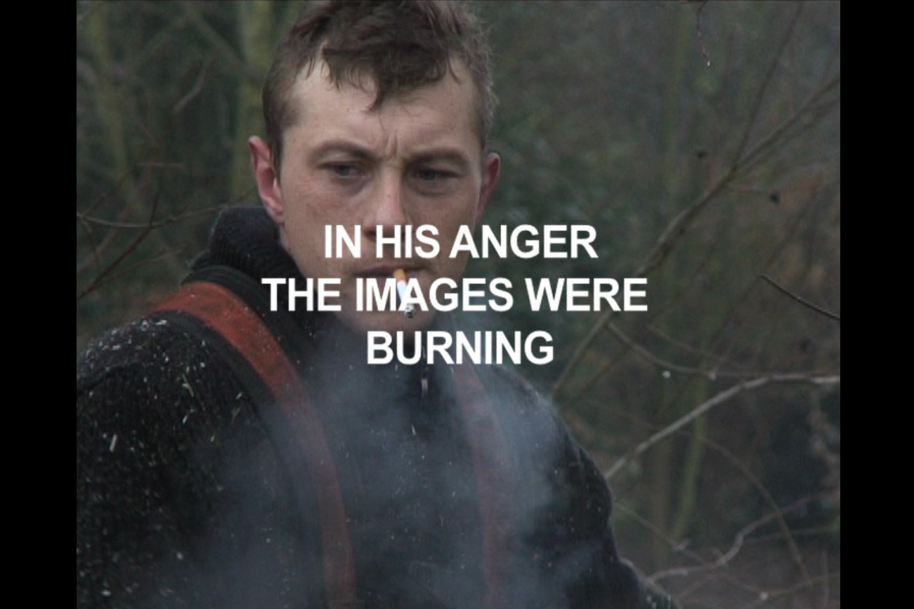 A man in the woods with a cigarette hanging from his mouth with white text over his face reading "in her mind the images were burning". 