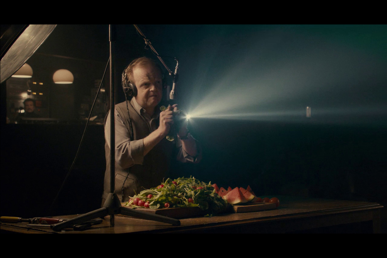 A foley artist ringing a piece of lettuce into a microphone over a pile of salad and a cut up watermelon. 