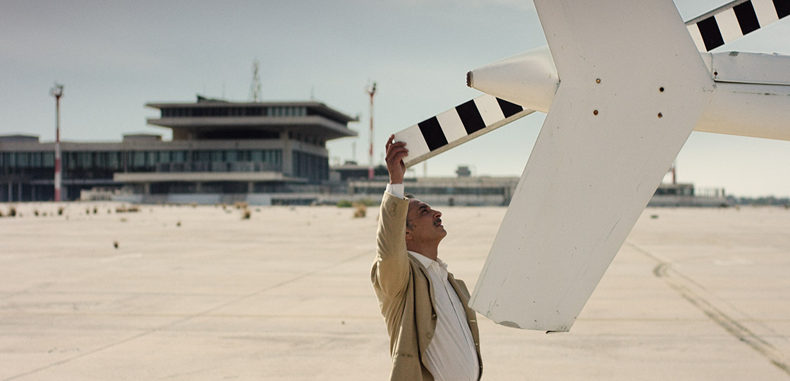 A lebanese man standing on a runway with his hand on a white helicopter rear propeller. 