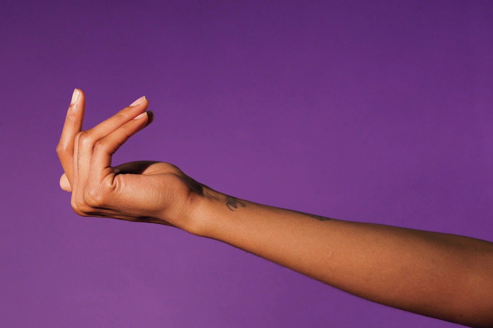An arm with an illegible tattoo on the wrist reaches across a purple background. 