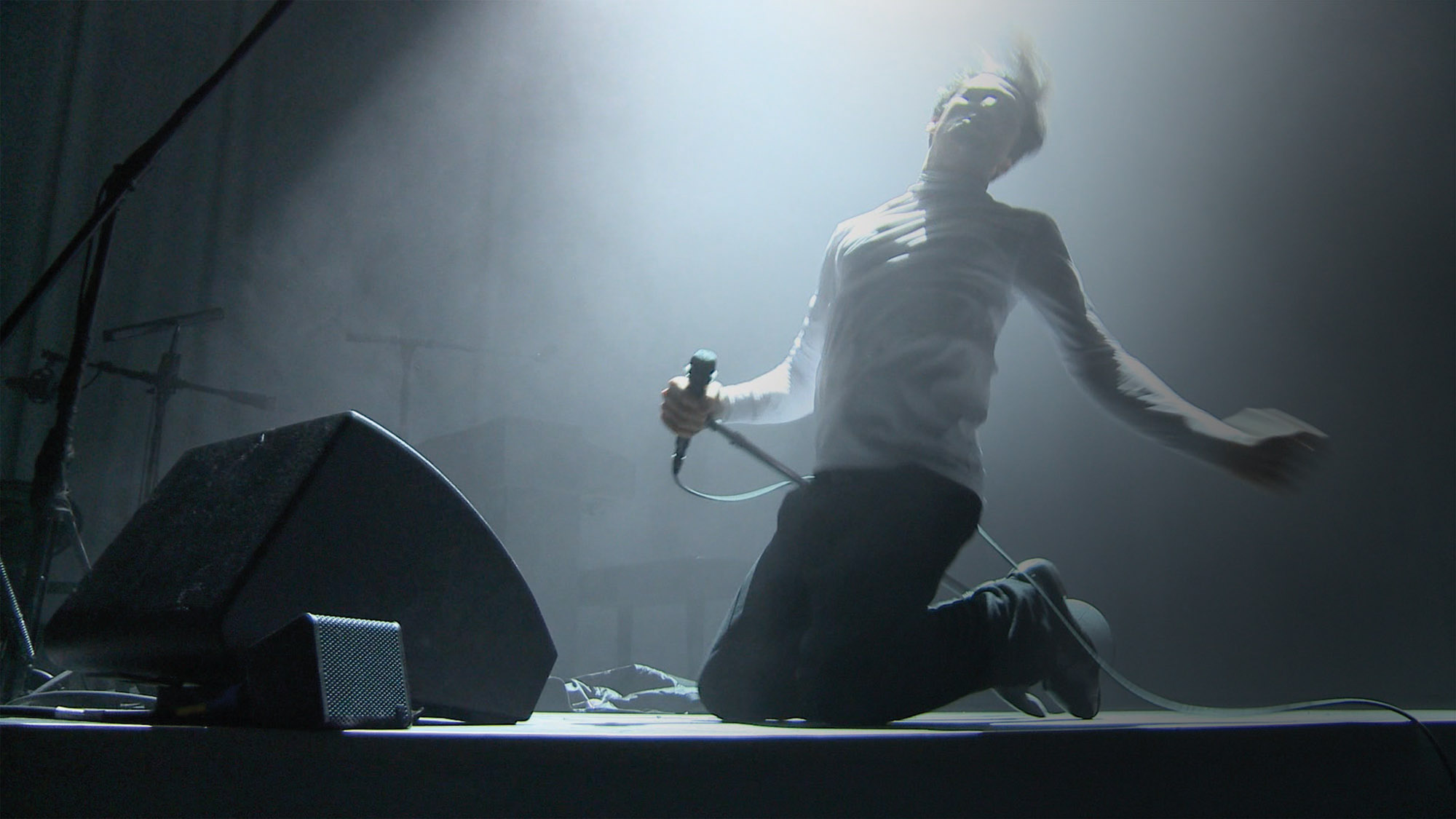 frances starlite holding a microhpone sliding on his knees to the end of the stage in light theatrical fog. 