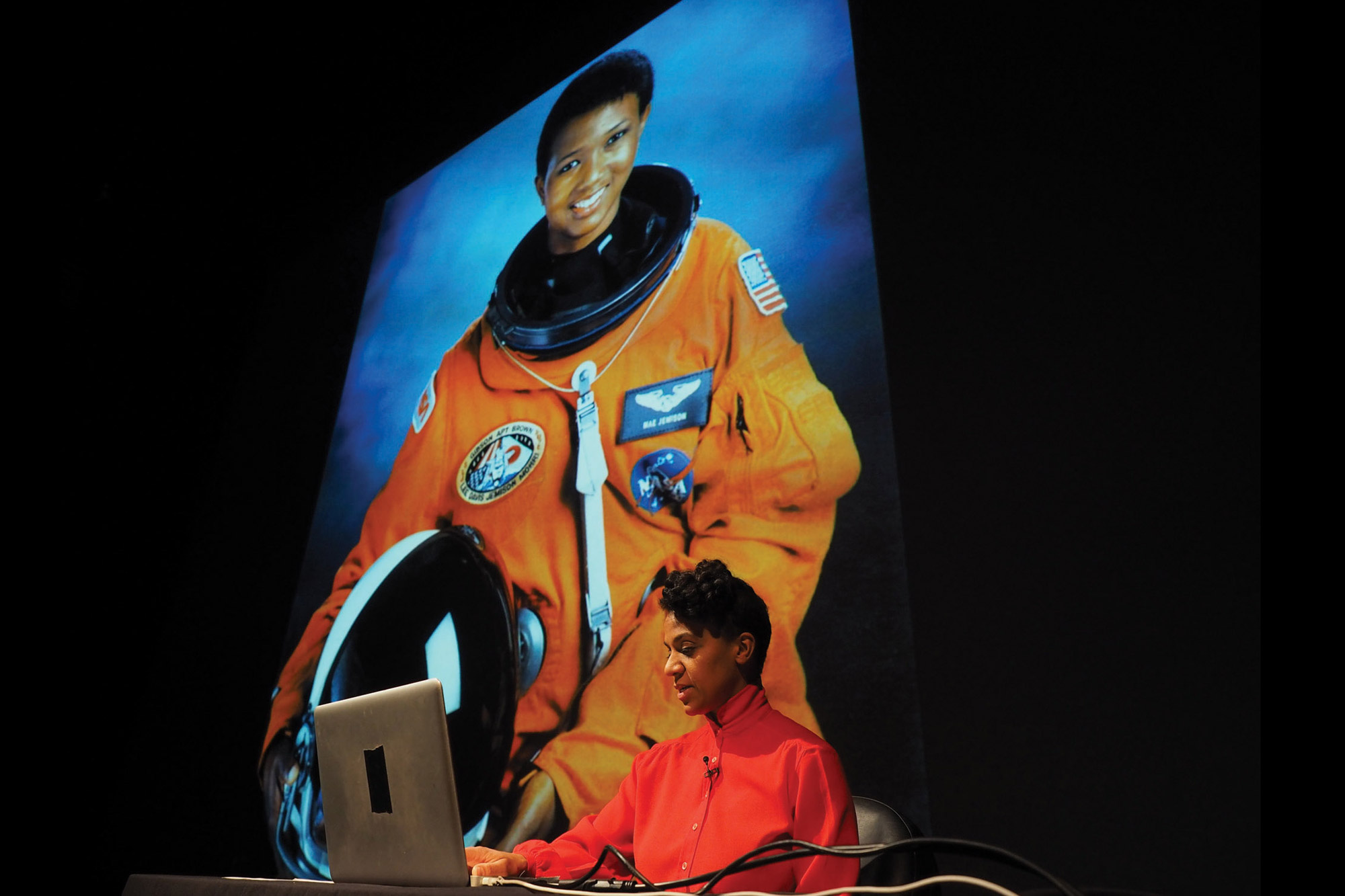 A projection of Mae Jemison in her nasa orange space suit. 