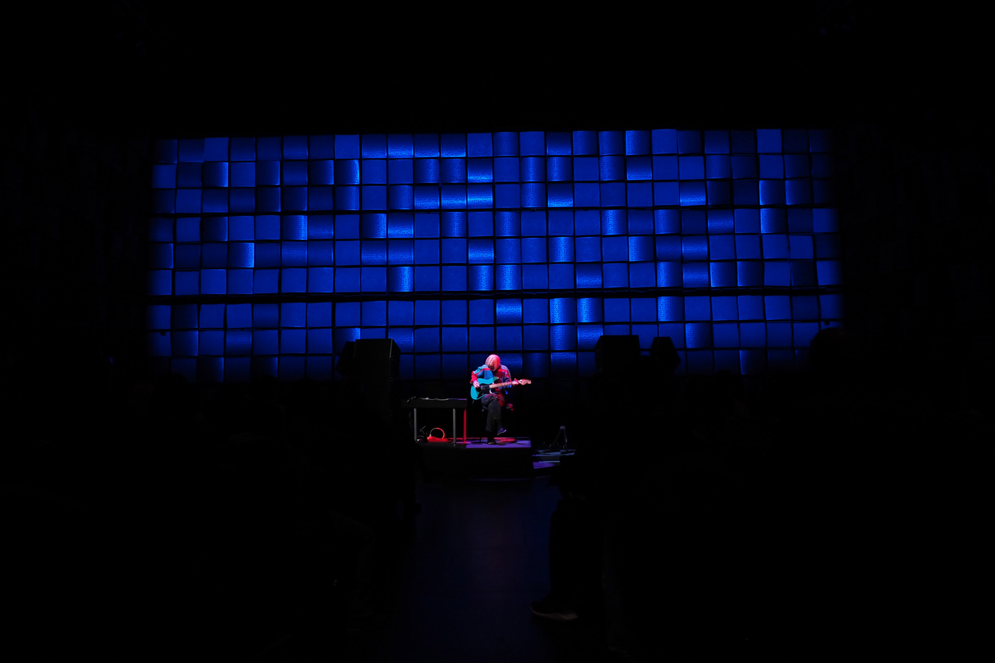 Ellen Arkbro playing an electric guitar on stage while washed in pink light in front of a grid of blue squares. 