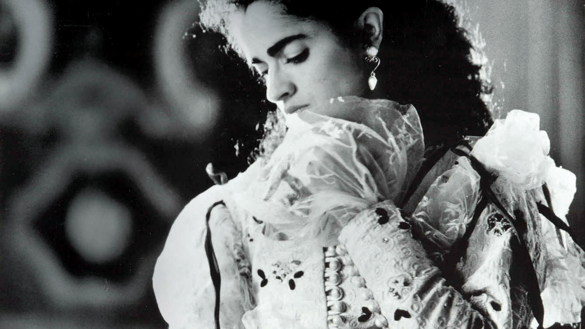 A woman wearing an ornate white dress with puffy sleeves and organza flares coming out of the bottom of the sleeve looking down over her shoulder dramatically. 