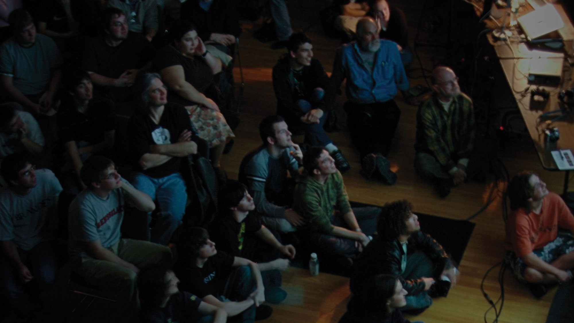 A captivated audience seated on the floor looking up at an unseen performance. 
