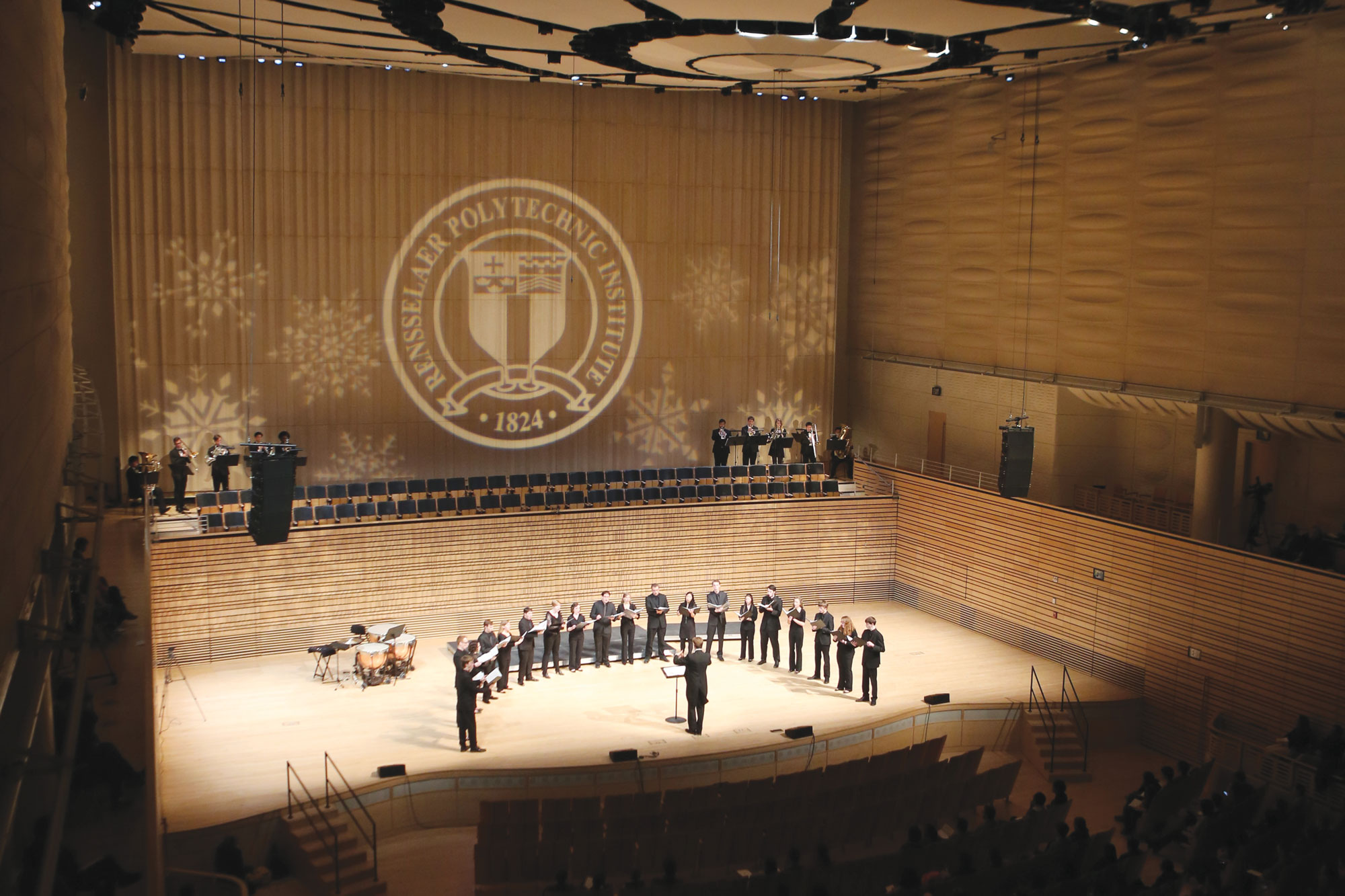 a student choir wearing black gathered in a semi circle on the concert hall stage. 