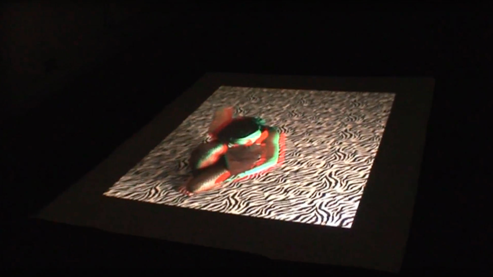 A dancer blurred with green and red shadow laying on their side on a zebra print floor. 