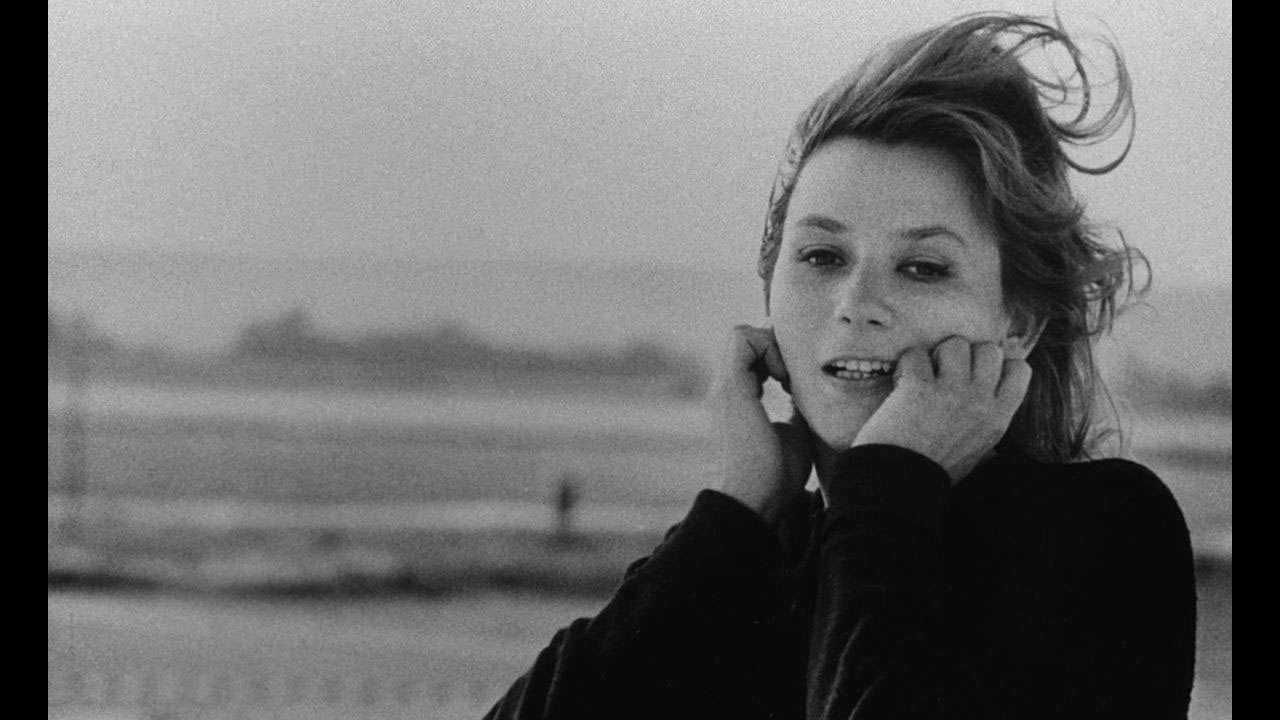 A white woman wearing a black turtleneck with windswept hair gently resting her face on her hands. 