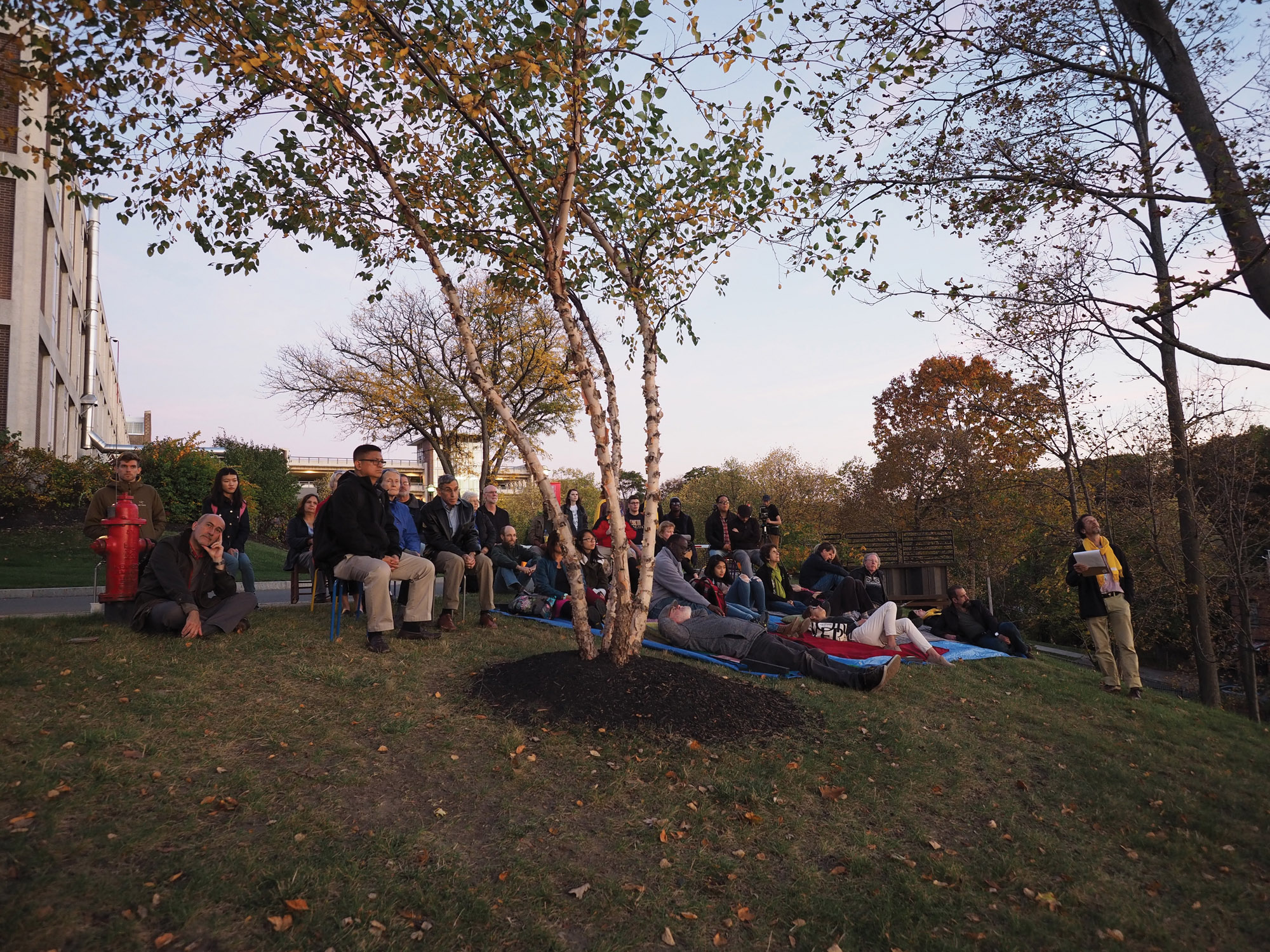 A group of people seated on blankets and lawn chairs on the side of the empac hill in the fall. 