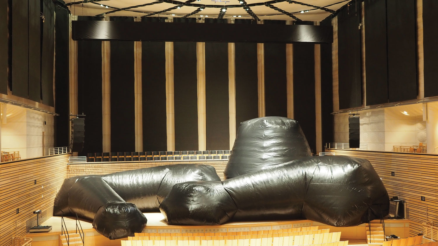 A black inflatable sculpture in an organic shape set up on the concert hall stage. 
