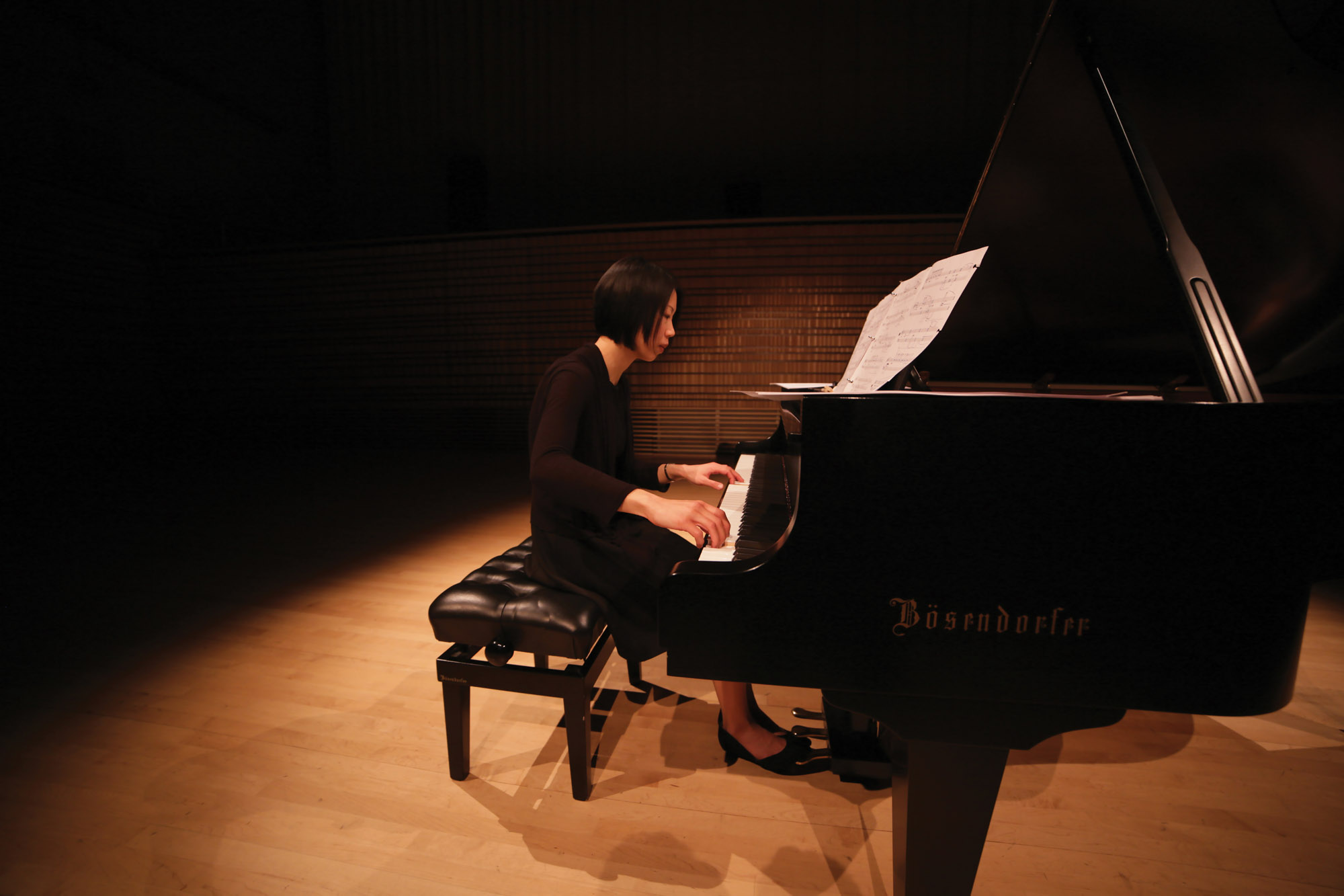 A woman playing a baby grand piano on the concert hall stage. 