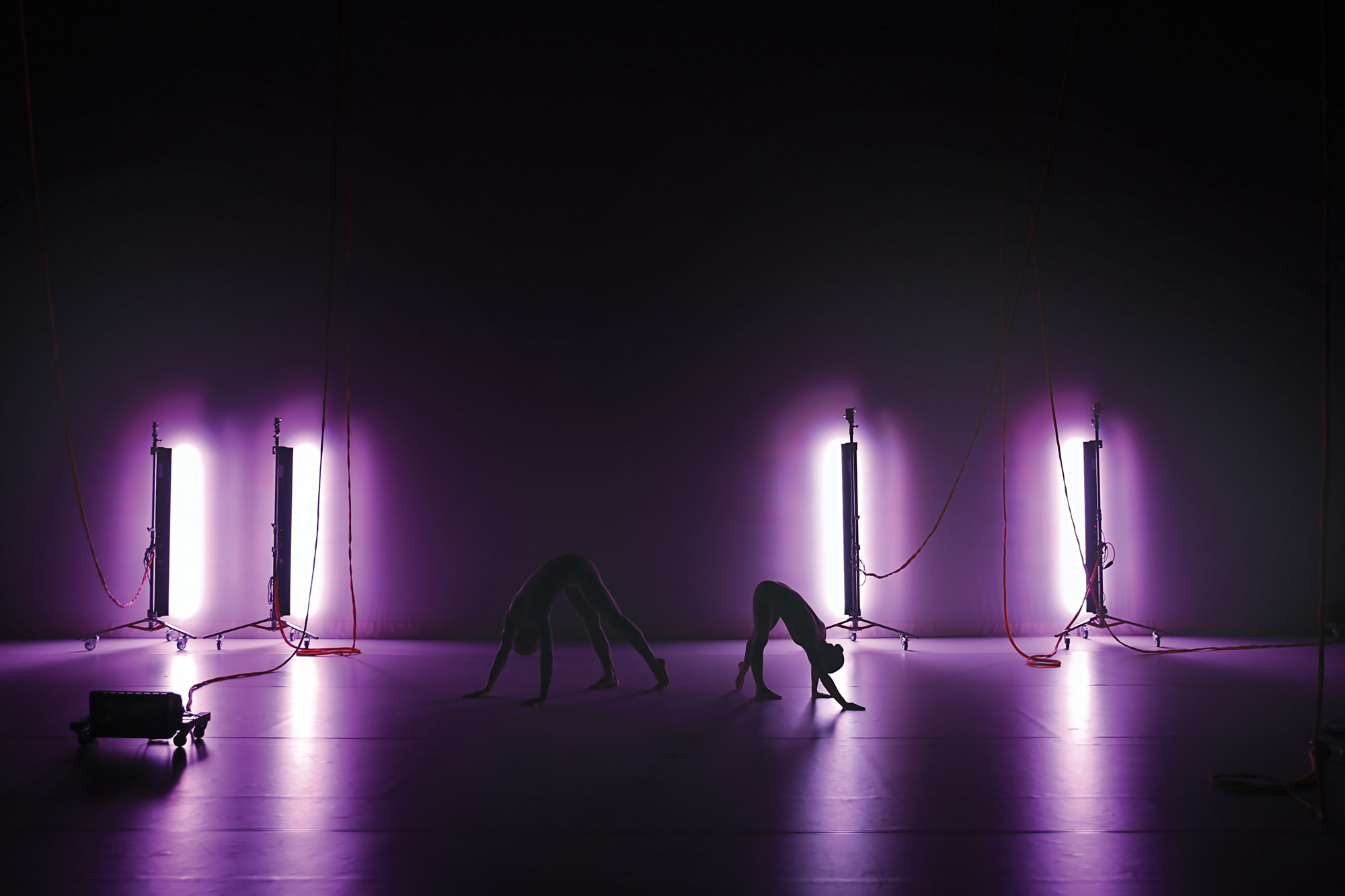 Two dancers in bent positions washed in purple light 
