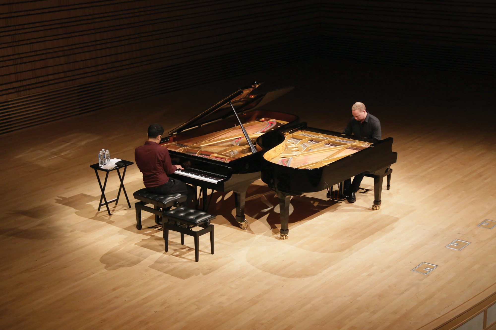 Two men playing two pianos next each other on the concert hall stage. 