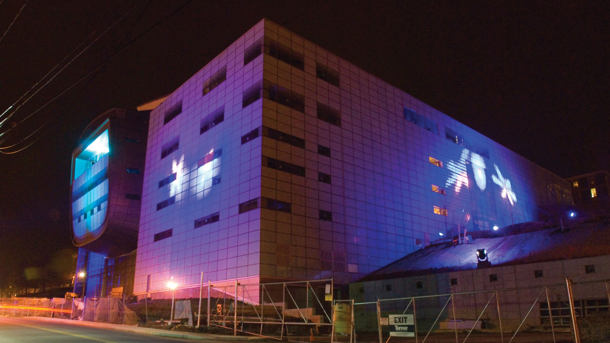 The exterior of EMPAC during construction lit at night with blue/purple lighting. 