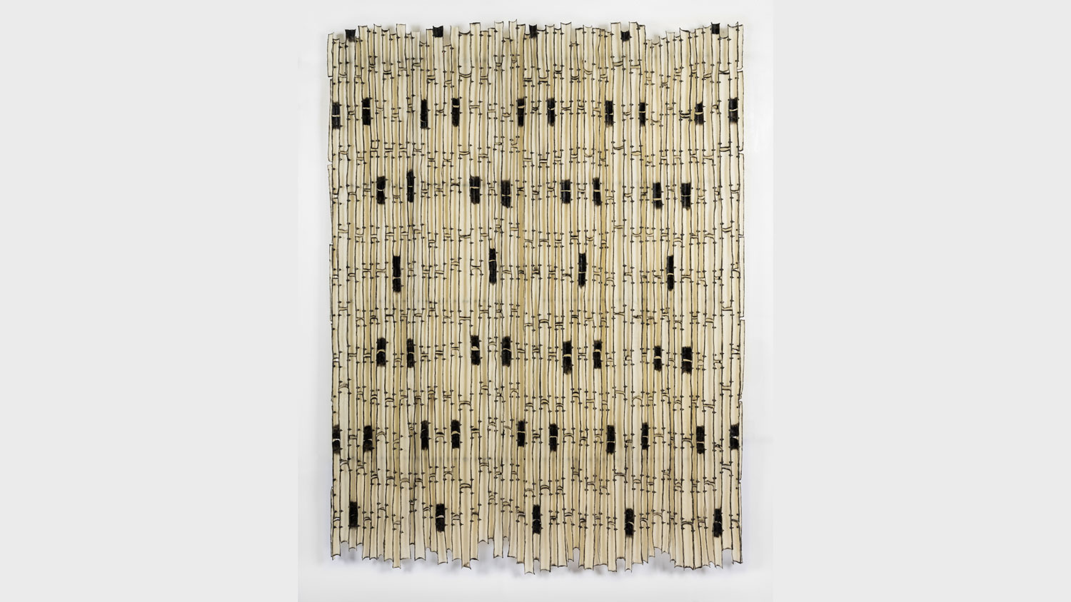 A birch tapestry of repeating patterns resembling bamboo hanging on a black white wall.  